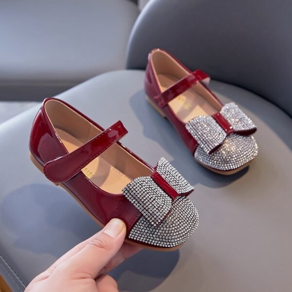 072261a4-56e2-4599-a334-7083320032fd.jpg حذاء مسطح من الجلد اللامع مزين بعقدة من أحجار الراين للفتيات الصغيرات